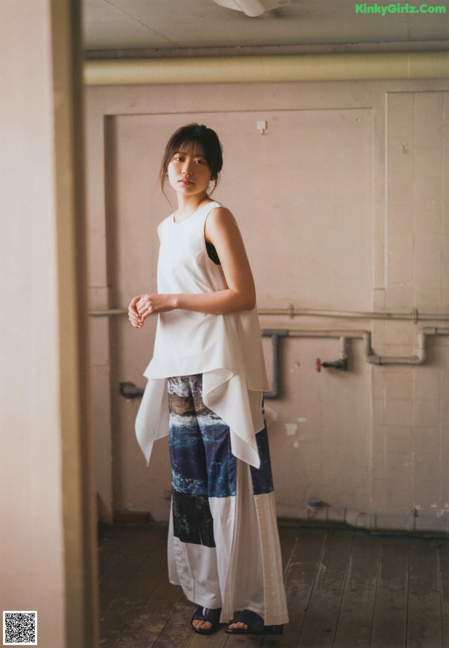 A woman standing in an empty room wearing a white top and blue pants.