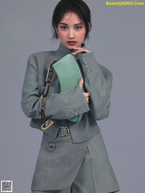 A woman in a gray sweater and black tights holding a handbag.