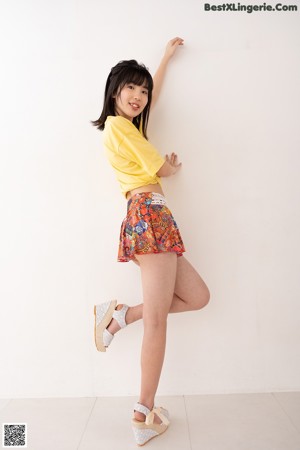 A young woman leaning against a wall in a yellow shirt.