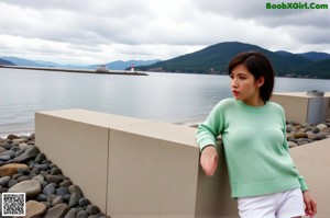 A woman sitting on a window sill wearing a green sweater.