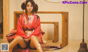 A woman in a pink kimono sitting on a wooden floor.