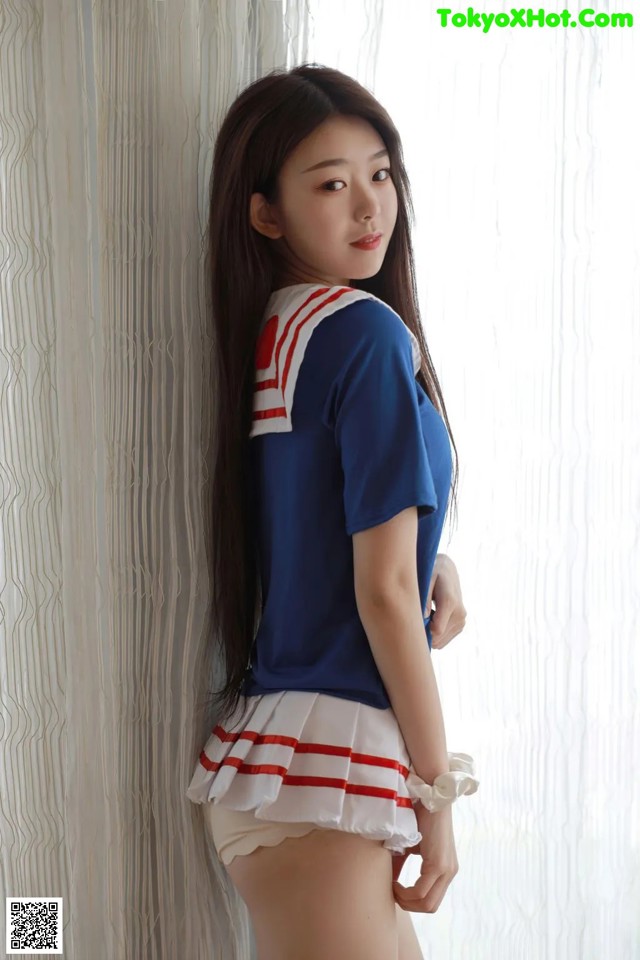 A woman in a sailor outfit leaning against a wall.