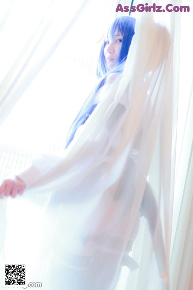 A woman with blue hair standing in front of a window.