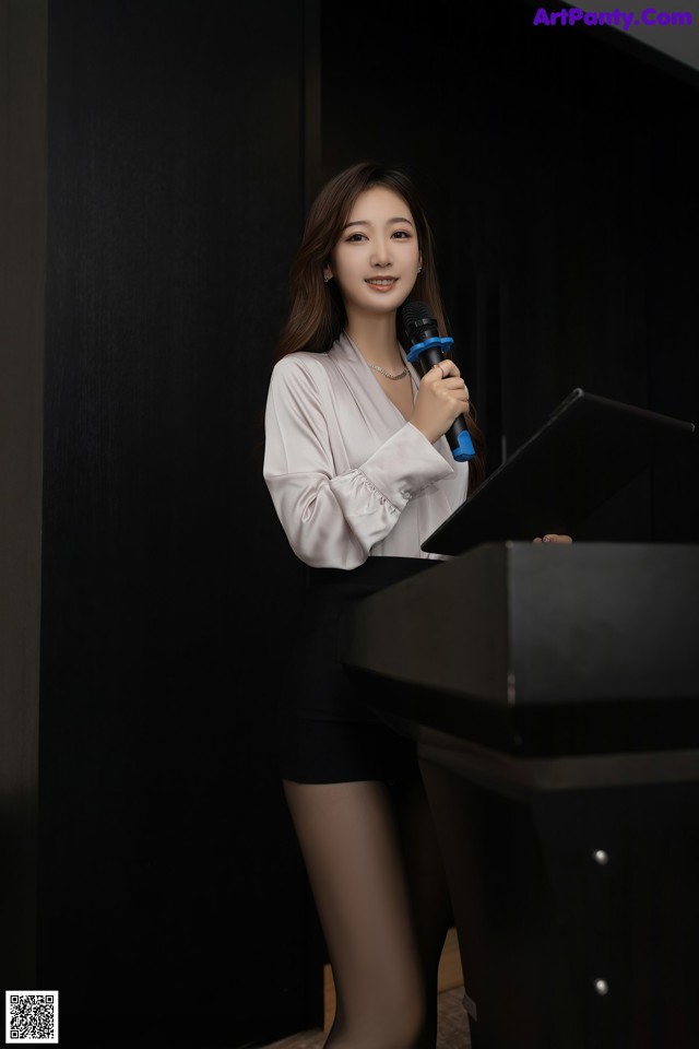 A woman standing at a podium holding a microphone.