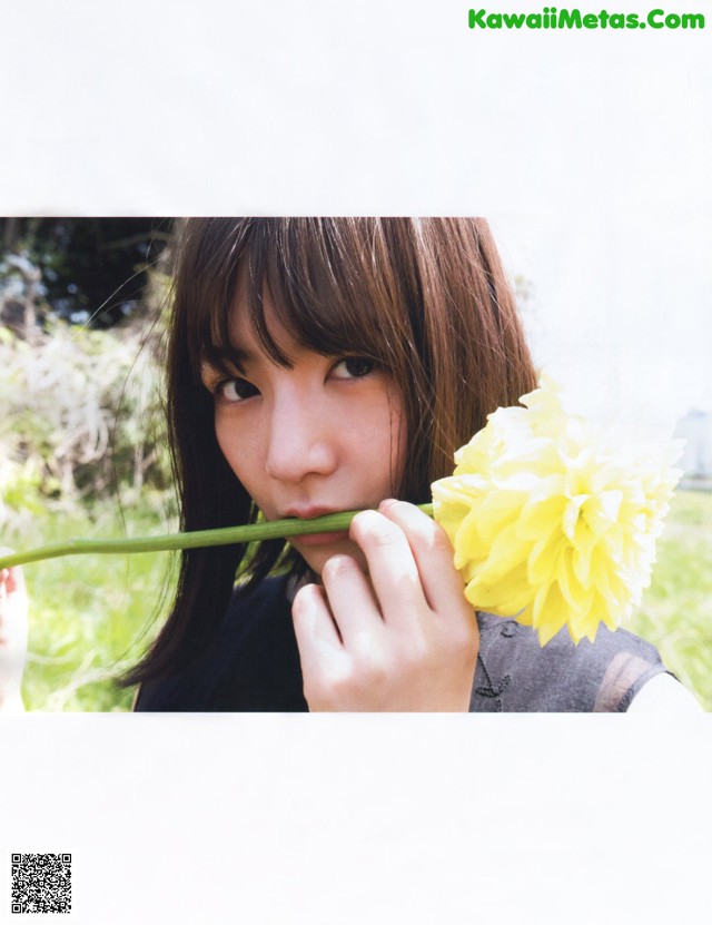 A woman holding a yellow flower in front of her face.