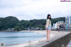 A young woman standing on a sandy beach with her arms outstretched.