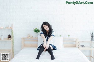 A woman in a school uniform sitting on a bed holding a sign.