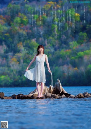 A naked woman standing on a beach next to a body of water.